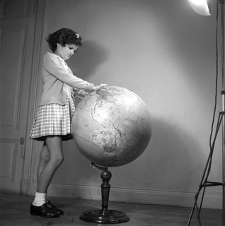 School in the 1940s. A girl in is very closely studying the details of a globe, something is