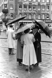 Umbrellas in the 1950s. A group of elderly women are standing together under their umbrellas. It's