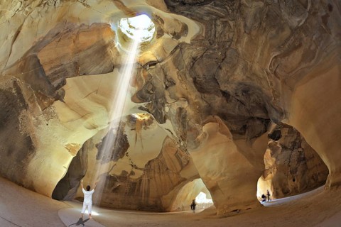 Yoga classes in the cave Beit Guvrin, Israel. Woman in white performs asana Sun salutation