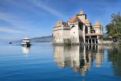 World-wide well-known Château de Chillon on Lake Geneva. The white tourist motor ship floats by a