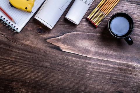 Checked copybook pencil blueprints measuring tape wooden meter and cup of coffee on pine wood board