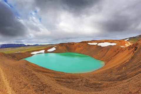Lake water bright green color. On the shores lie snowfields from last year. Picturesque lake in the