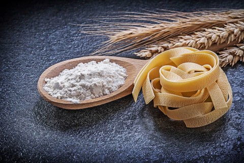Wheat rye ears wooden spoon flour pasta on black background
