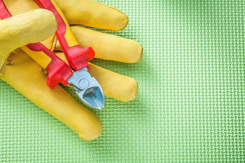 Yellow protective gloves sharp nippers on green background electricity concept