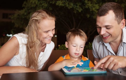 Young parents and little son in a cafe in the evening. Father and son using touch pad, mother