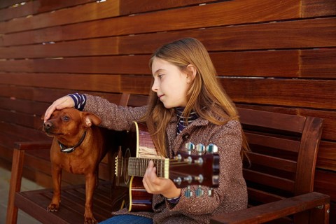 Blond kid girl playing guitar with dog and winter beret on wooden background