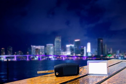 Car rental keys on wood table with blank paper in Miami night downtown