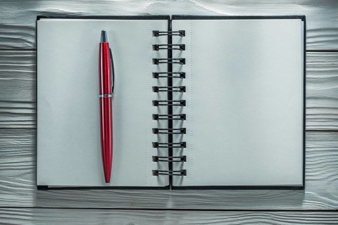 Opened notebook pen on white wooden board