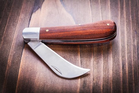 Opened agricultural knife on vintage wooden board close up