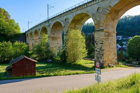 A massive stone viaduct towers over a green landscape with a small country road in the foreground,