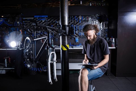 Stylish man with beard, cycle mechanic takes notes, checklist before repairing and servicing bike