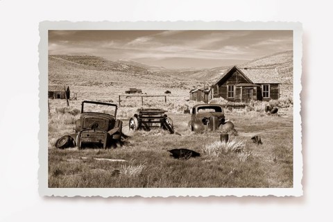 Several rusting car wrecks in a meadow in front of a wooden house in the former gold mining town of