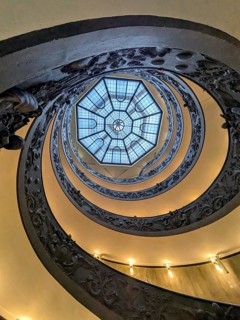 View from below of an ornate spiral staircase with a geometric skylight at the top, showcasing