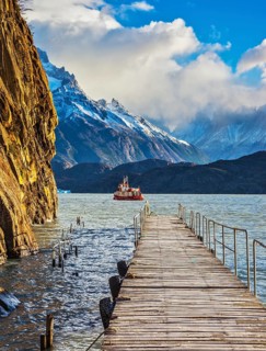 Pleasure boat for tourists swim with wooden pier. Grey Lake in the national park Torres del Paine,
