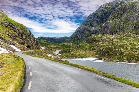 Narrow dangerous mountain road glitters from the rain. The roadside is marked with high poles.