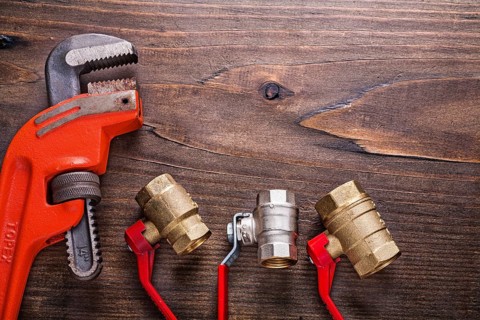 Plumbers fixtures with red handles and monkey wrench on vintage wooden board with copyspace