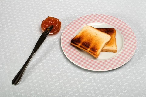 Slice of bread spread with jam and knife on a small bowl