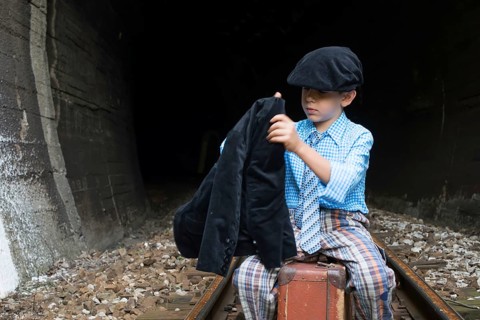 Child in vintage clothes sits on railway road in front of a tunnel