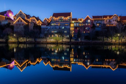 Christmas illuminated house facade of Frohnleiten reflected in the river Mur, blue hour,