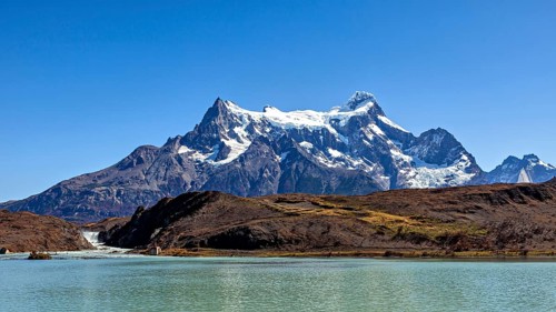 Snowy mountain above a calm river and turquoise water under a blue sky, The landscape of the Torres