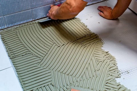 A tiler at work. Gluing floor tiles with tile adhesive and trowel. Austria