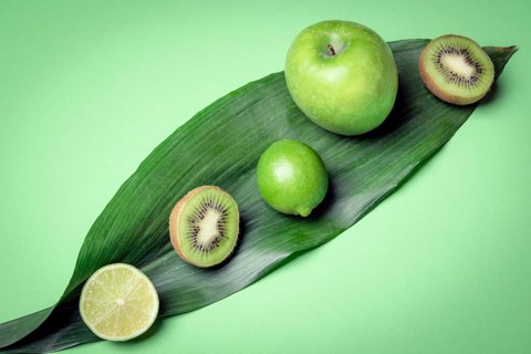 Mix of raw fruits on a green leave. Green kitchen table with fresh detox fruits