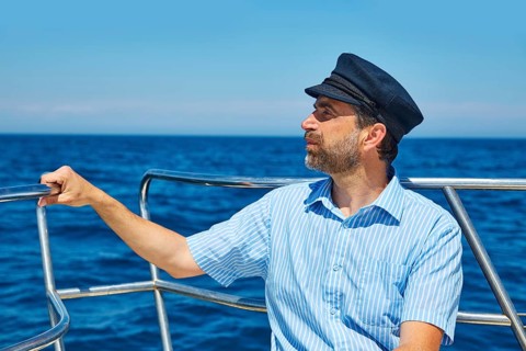 Beard sailor man sailing sea ocean in a boat with captain cap looking horizon