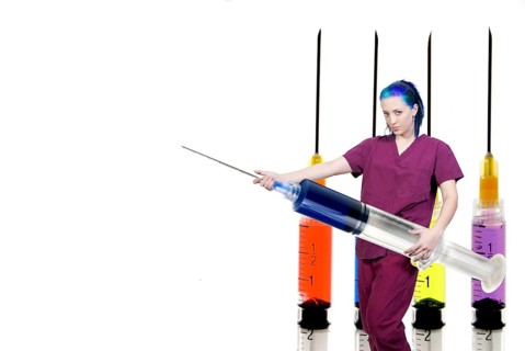A medical doctor or nurse in scrubs preparing an injection in a giant syringe