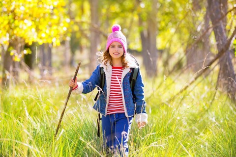 Hiking kid girl with backpack in autum poplar trees forest and walking stick