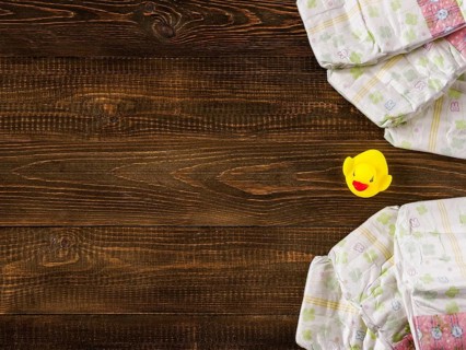 Japanese disposable diapers and the rubber duckling on dark wooden background with copy-space. Flat
