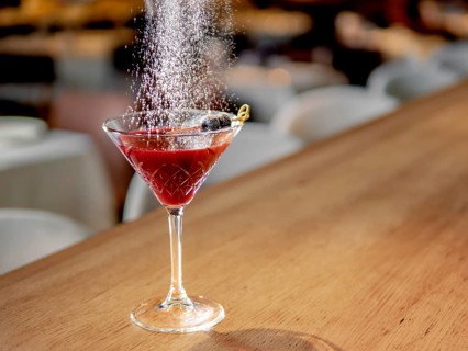 Red cocktail in martini glass on bar counter. White powdered sugar sprinkled on alcohol cocktail