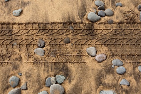 Car tire footprint in a sand and rolling stones beach texture