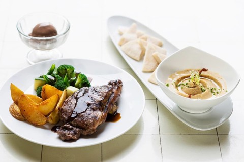 Grilled steak meal with hummus dip starter on table