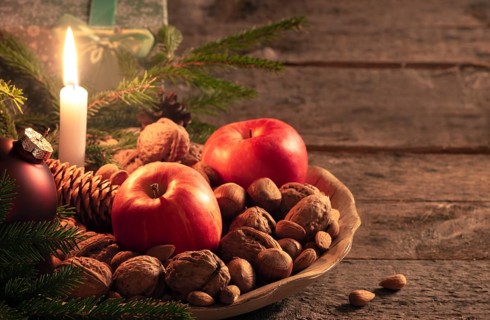 Christmas scenery with a wooden platter full of walnuts, hazelnuts and apples, green fir twigs and