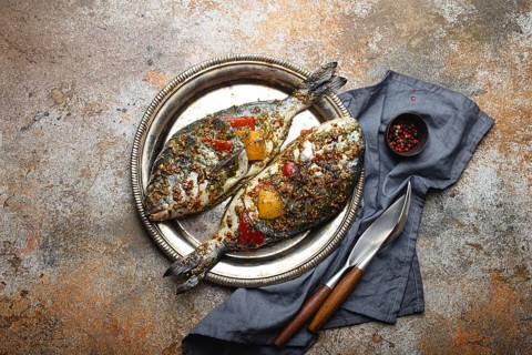 Two raw fishes dorado stuffed with vegetables and seasonings ready to be cooked laying on rustic