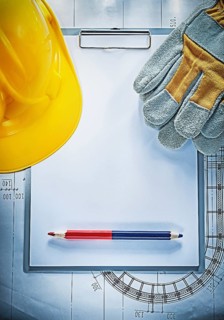 Clipboard pencil building helmet safety gloves on blueprint construction concept