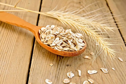 Rye flakes in wooden spoon, rye stalks on a wooden boards background