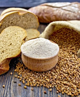 Buckwheat flour in a wooden bowl, buckwheat in the bag, the bread slices on a wooden boards