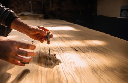 Person using tools on wood in a workshop with warm sunlight creating a focused and serene