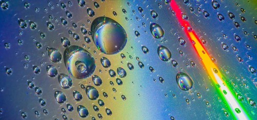 Beautiful closeup of water droplets floating on blueish silver background with rainbow colors