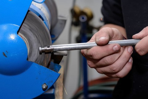 Skilled worker working on metal on a bench grinder - close-up