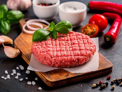 Close up view of two raw meat steak cutlets for burger with vegetables, spices and fresh basil.