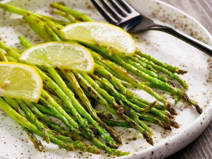 Close up view of grilled asparagus and slice of lemon in craft trendy plate on brown wooden table
