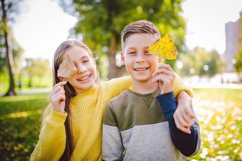 Happy twins teenagers boy and girl posing hugging each other in autumn park holding fallen yellow