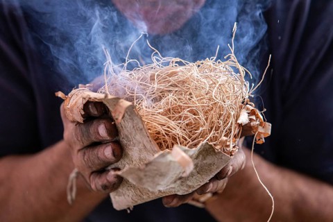 Closeup of man hand holding straw used as fire starter with smoke during demonstration of native