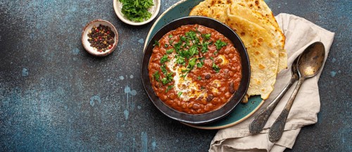 Traditional Indian Punjabi dish Dal makhani with lentils and beans in black bowl served with naan