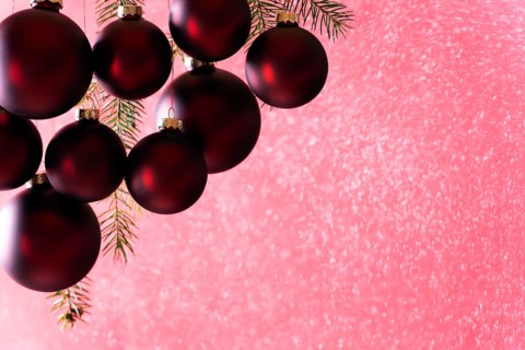 Elegant dark red Christmas balls hanging while snowing, from a snow spray, in bright light, perfect
