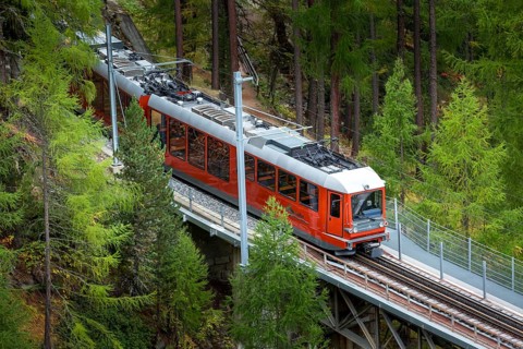 Zermatt, Switzerland, October 7, 2019: Gornergrat red tourist train on the bridge, village houses