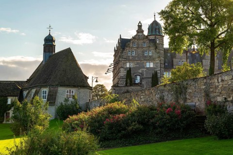 Historic Hämelschenburg Castle with castle church, well-tended garden and old walls in the evening