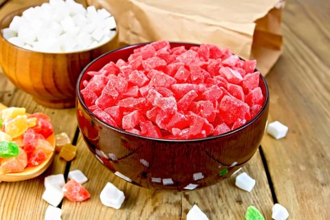 Candied papaya and coconut in bowls, colorful pieces of candied fruit in a spoon on a wooden boards